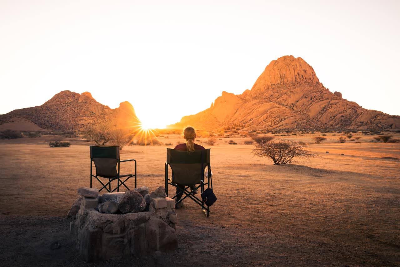 Two camping chairs beside a fire pit at sunset below Spitzkoppe